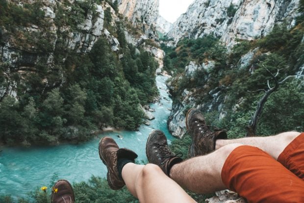 legs dangling over a cliff looking over a river